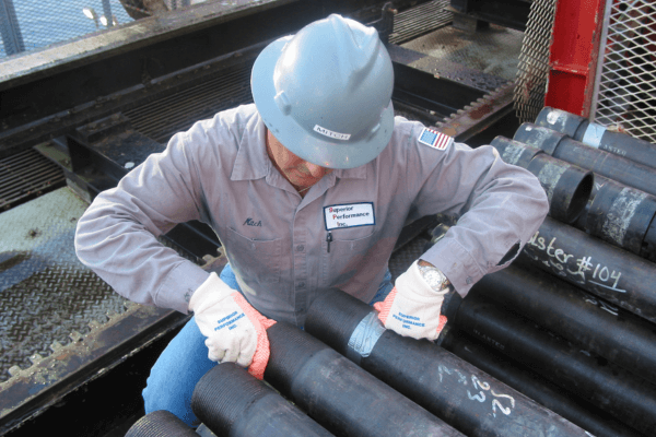 A worker wearing a grey hard hat and a Superior Performance FR clothing expecting a piece of pipe on an offshore oil rig  (1)
