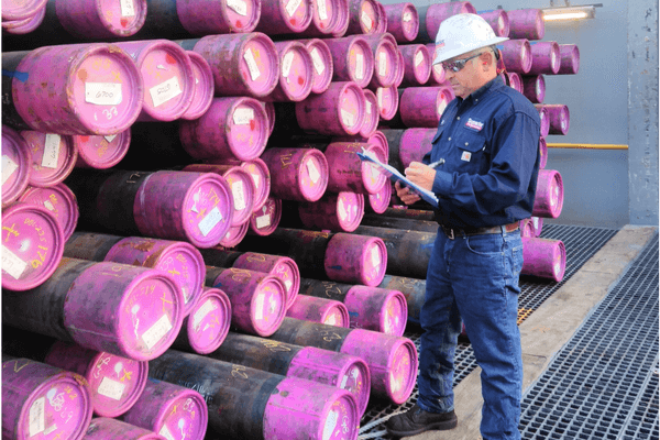 Industrial technician inspecting stacked tubulars during inventory and quality control representing tubular management services.